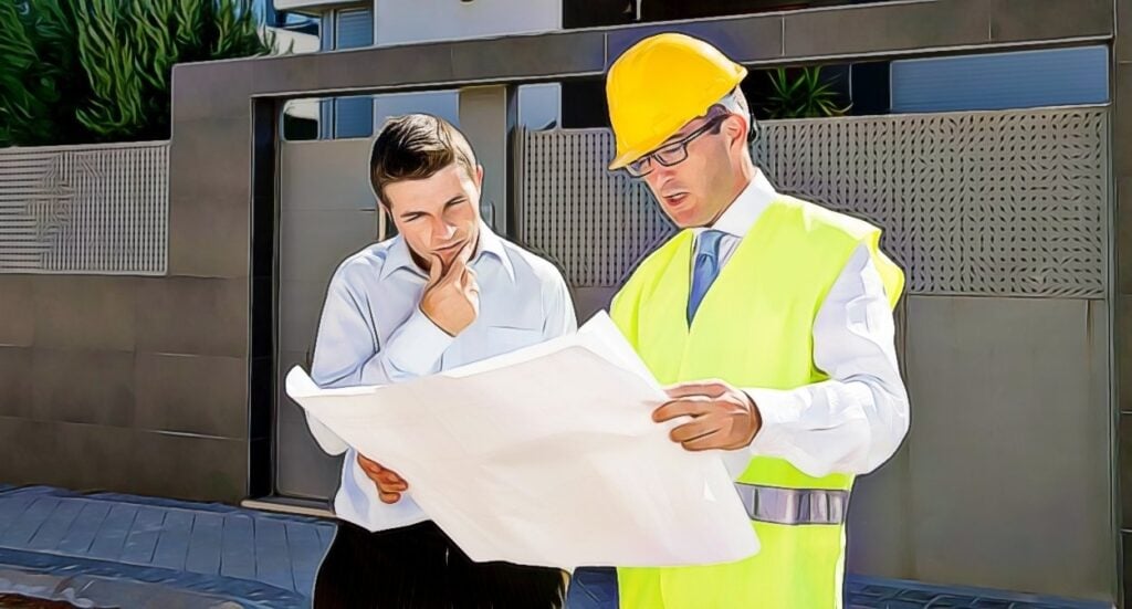Two men stand outside a building, reviewing large blueprints; one wears a yellow safety vest and hard hat, while the other, in a dress shirt, looks thoughtfully at the plans.