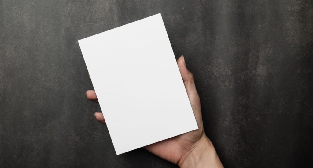A hand holding a blank white rectangular card against a dark, textured background.