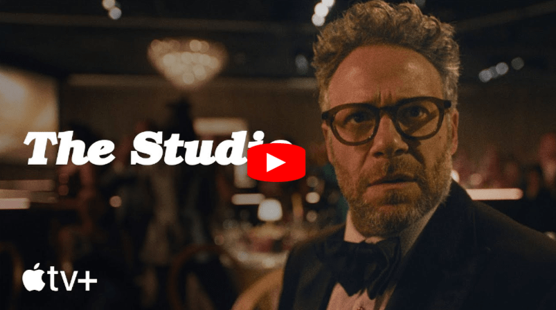 A man wearing glasses and a tuxedo looks surprised in a dimly lit, elegant room. The words The Studi and the Apple TV+ logo appear, with a red YouTube play button in the center.