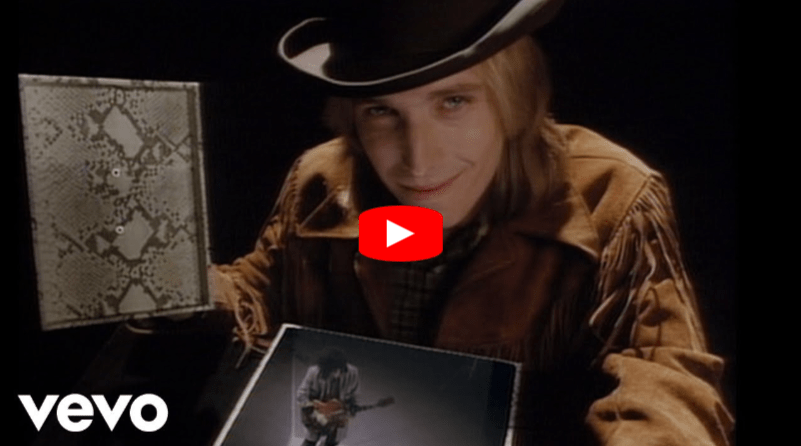 A man in a cowboy hat and fringed jacket smiles while holding open a book. In front of him is a photo of a guitarist. The Vevo logo and a play button overlay are visible.