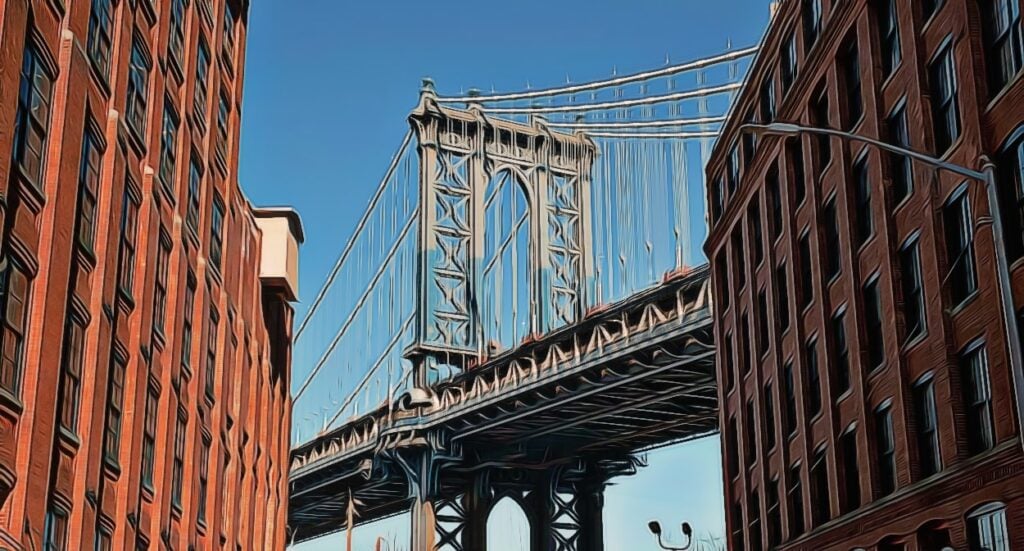A view of the Manhattan Bridge framed by tall red brick buildings on either side, under a clear blue sky.