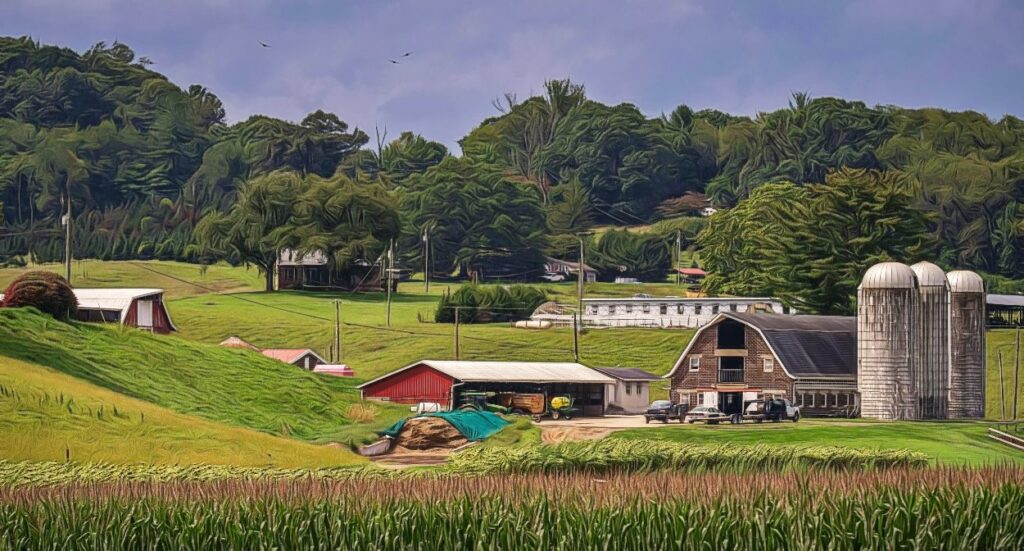 A scenic view of a rural farm with barns, silos, parked vehicles, green fields, and trees under a partly cloudy sky, surrounded by rolling hills and a cornfield in the foreground.