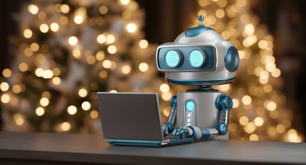 A cute, blue and silver robot sits at a table using a laptop, with warm, blurry holiday lights and a decorated Christmas tree in the background.