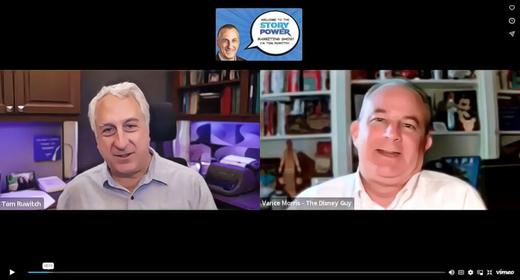 Screenshot of a video call featuring two men, Tom Ruwitch and Vance Morris—The Disney Guy, both smiling. The background includes bookshelves and office decor. The video title at the top reads Welcome to the Story Power Marketing Show.