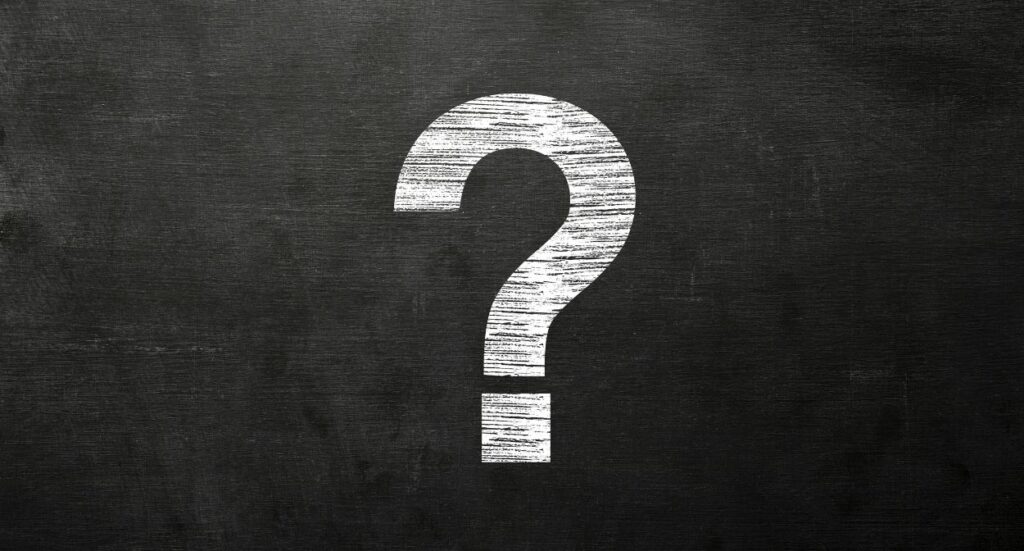 A large white question mark is drawn on a black chalkboard background, with visible chalk texture and smudges around the mark.