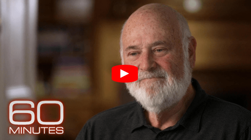 A bearded older man smiles while seated indoors, with soft lighting in the background. The 60 Minutes logo appears in the lower left, and a red play button is centered, indicating this is a video thumbnail.