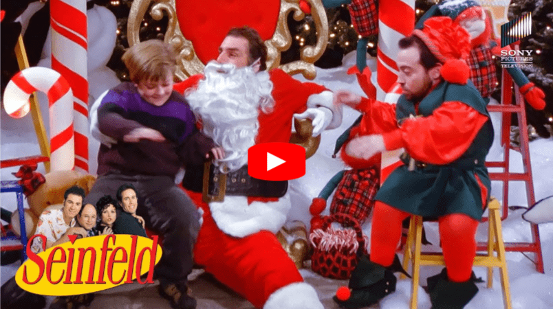 A boy sits on Santaās lap next to a man dressed as an elf at a Christmas display. The Seinfeld logo appears in the corner with an inset of the main cast. A play button overlays the center.