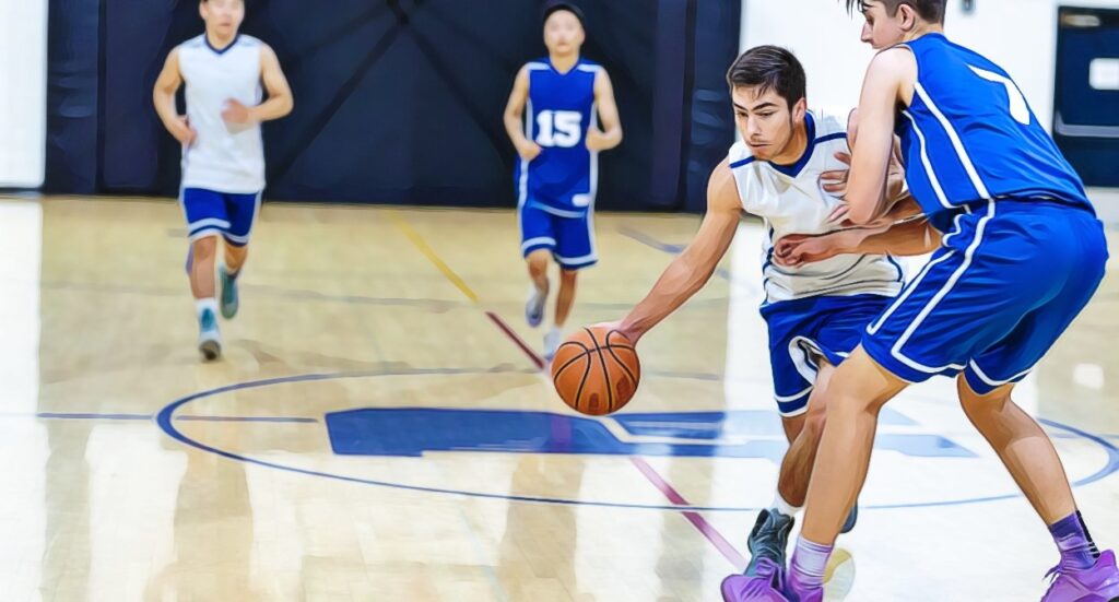 A basketball player in a white jersey dribbles the ball while being closely guarded by a player in a blue jersey during a game on an indoor court. Two other players run in the background.