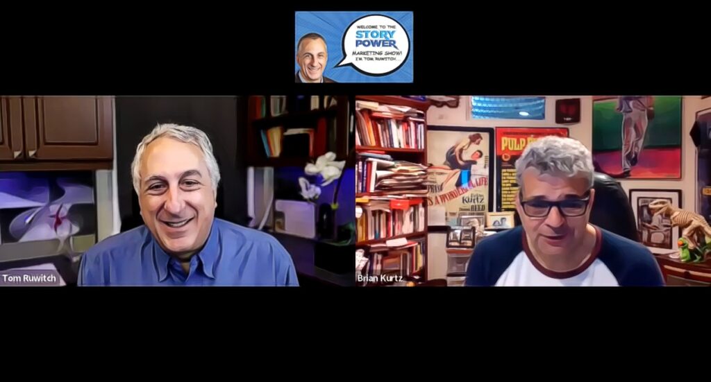 Two men, Tom Ruwitch and Brian Kurtz, talk via video call. Tom, smiling, is on the left in a blue shirt with books and a plant behind him. Brian, wearing glasses, is on the right in a room filled with books and posters.