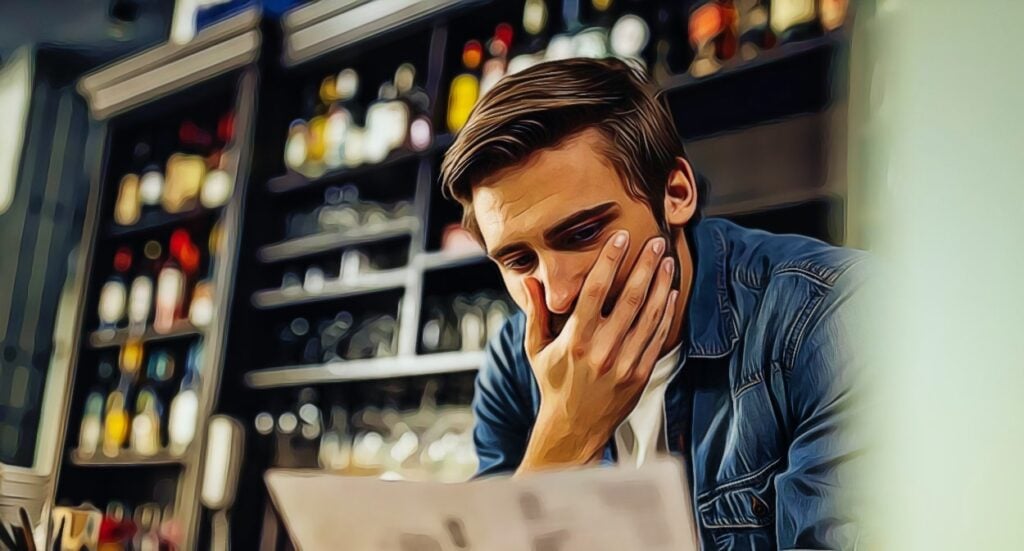 A man sits in front of shelves filled with bottles, looking concerned as he reads a piece of paper and covers part of his face with his hand. The image has an artistic, painted effect.