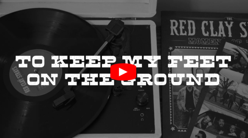 A black and white image of a vinyl record player, a partially visible album cover reading The Red Clay in the corner, and song lyrics TO KEEP MY FEET ON THE GROUND overlaid with a play button icon.